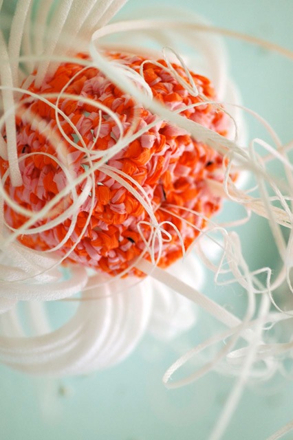 Detail of crochet coral sculpture in front of blue wall.