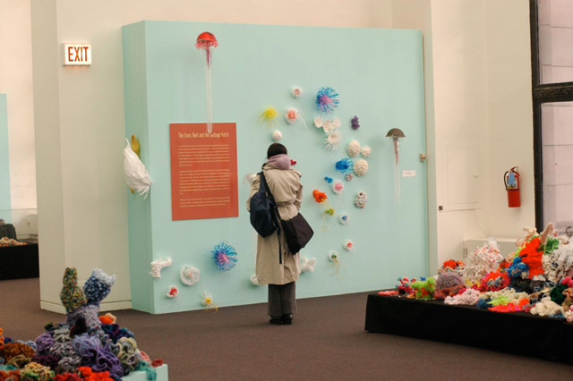 Person looking at crochet sculptures on the wall.