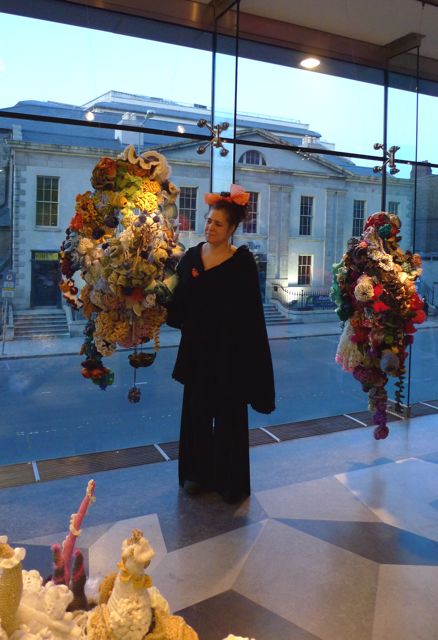 A woman making adjustments to hanging crochet coral reef sculptures.