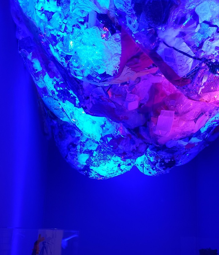 fishing net full of plastic trash hanging from gallery ceiling