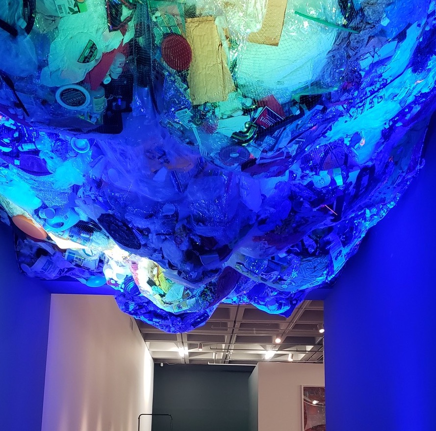 fishing net full of plastic trash hanging from gallery ceiling