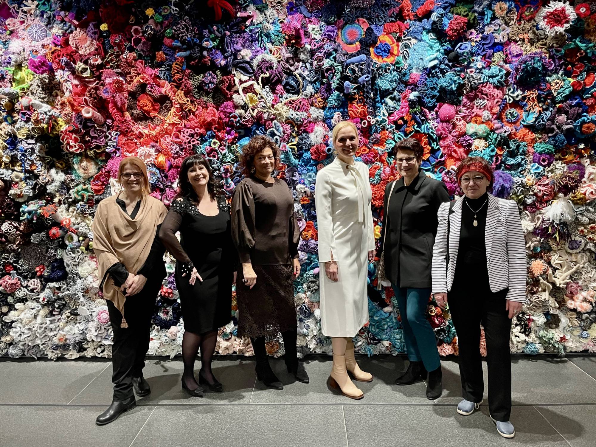6 women standing in front of a wall of crochet corals at museum